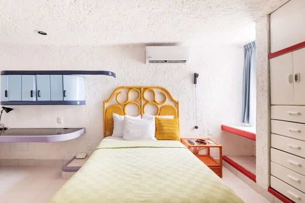 Dormitorio moderno con cama de plataforma de madera, TV montada en la pared, grandes ventanales con vistas a plantas tropicales y al océano.