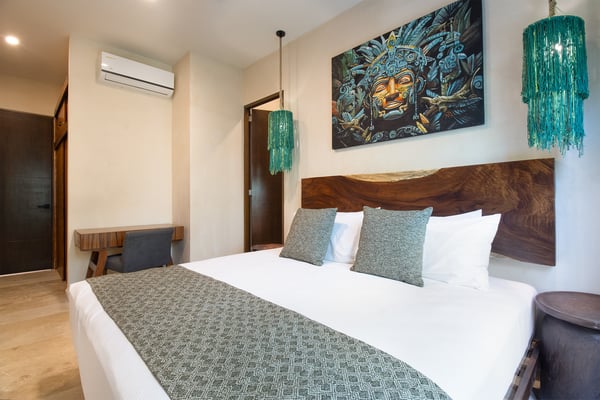 Modern bedroom with wooden platform bed, wall-mounted TV, large windows overlooking tropical plants and ocean view.