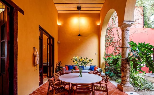 Dormitorio con cama queen que da a un patio cubierto con sillas de diseño coral y vistas a un jardín tropical